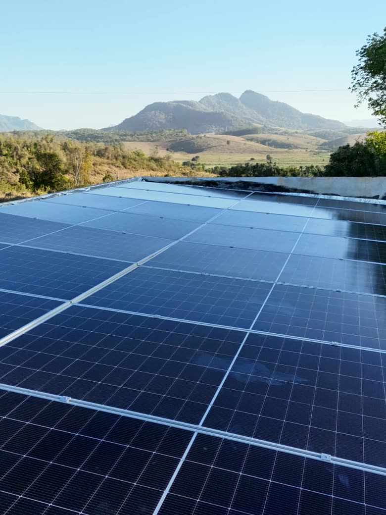 Telhado de galpão inteiramente coberto por placas solares, com montanhas ao fundo
